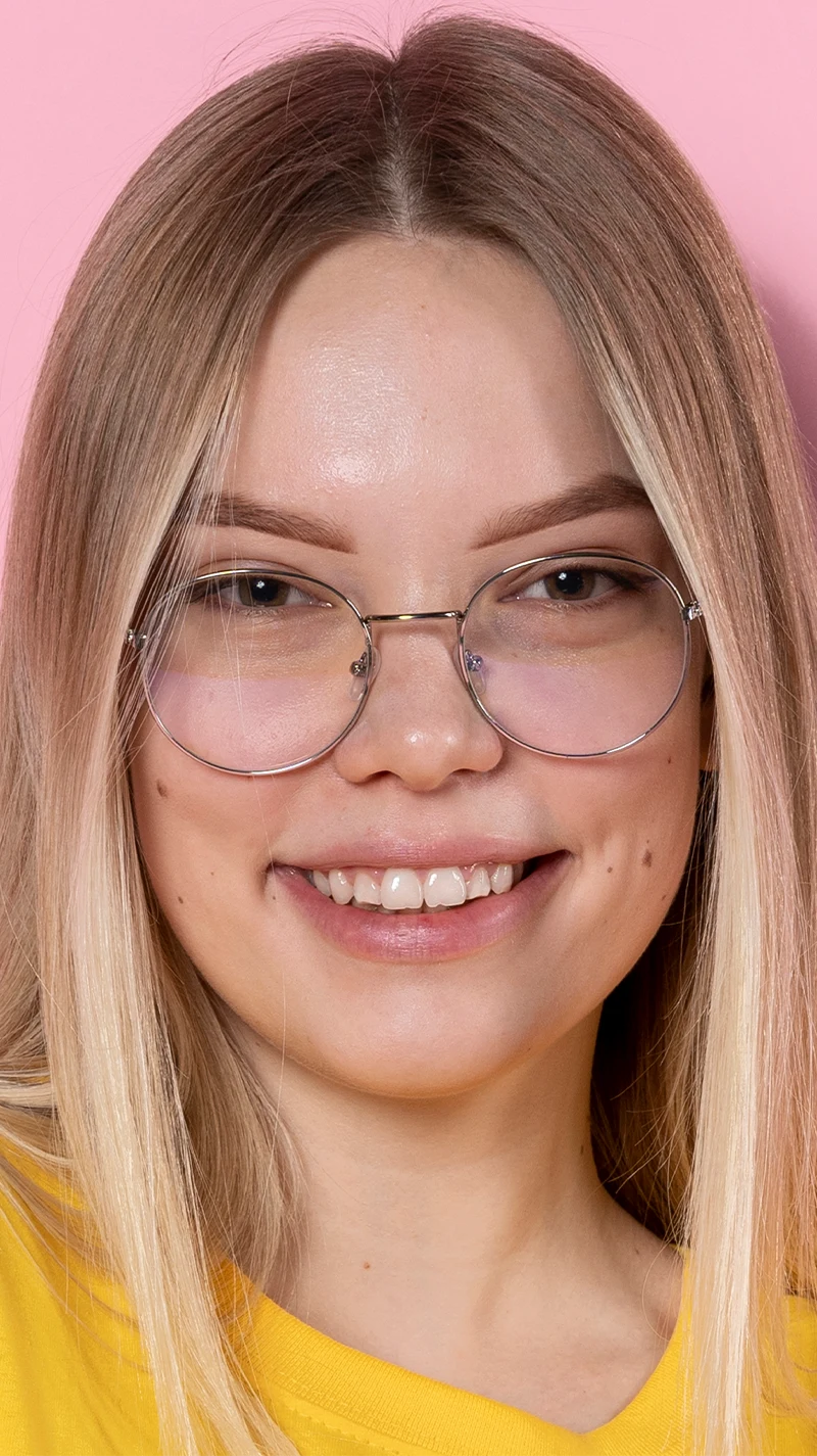 Eine junge, blonde Frau lacht in die Kamera. Sie trägt eine schmale, silberne Brille
