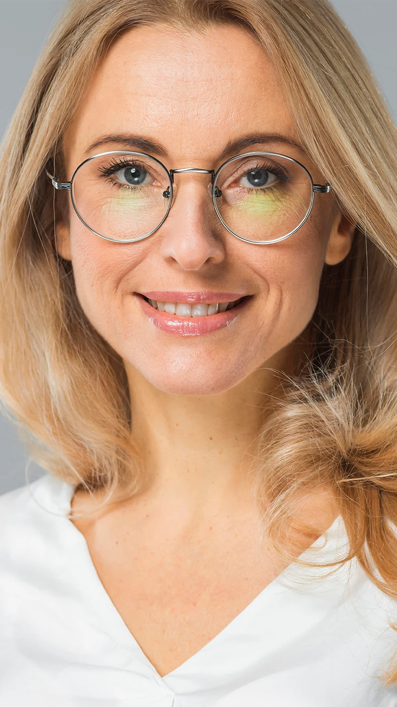 EIne blonde Frau, blickt mit einem Lächeln in die Kamera, sie trägt eine schmale, silberne Brille