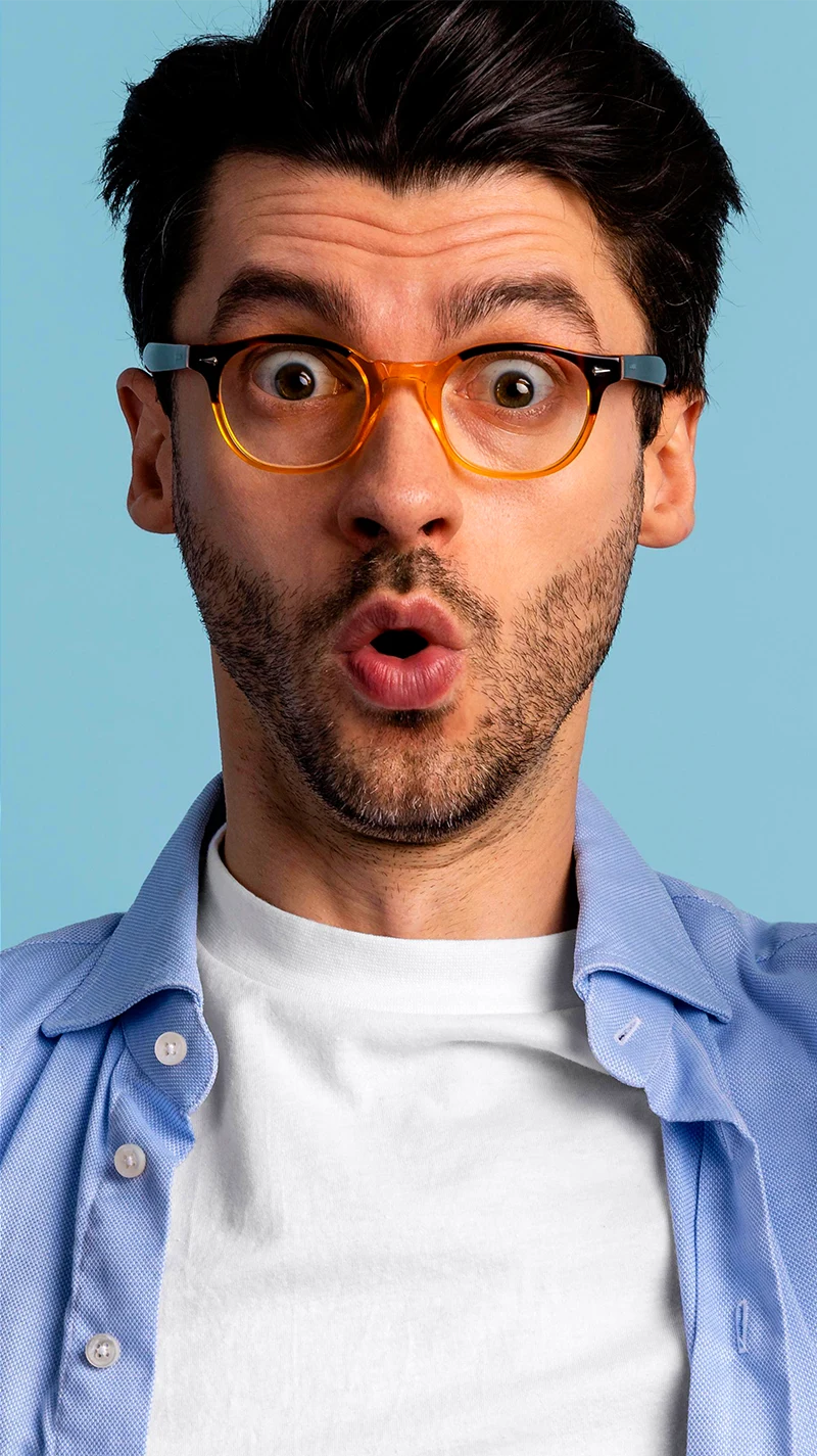Ein junger Mann sueht überrascht in die Kamera, er trägt eine bunte Brille